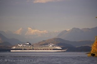A cruiseship passes by the mountainous landscape that shines in the sunlight off Northern Vancouver Island in British Columbia, Canada.